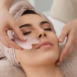 Young woman receiving facial massage with gua sha tool in beauty salon